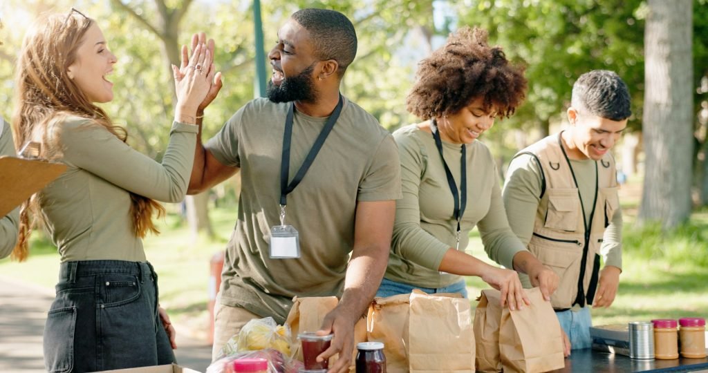High five, team and food for charity and nonprofit, package and meal for homeless in park. Kindness